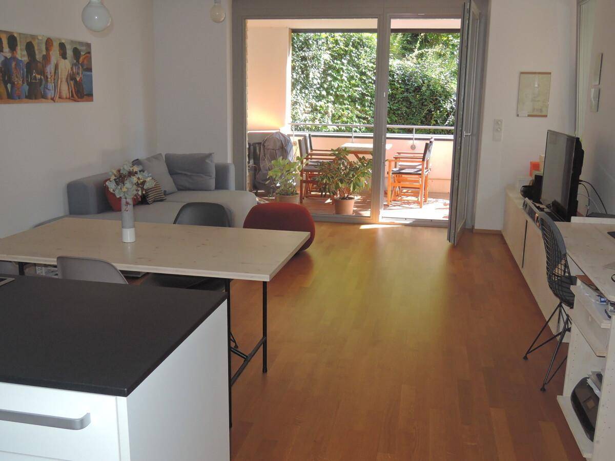 Heller Wohn- und Essbereich mit Holzboden und direktem Zugang zu einem möblierten Balkon.
