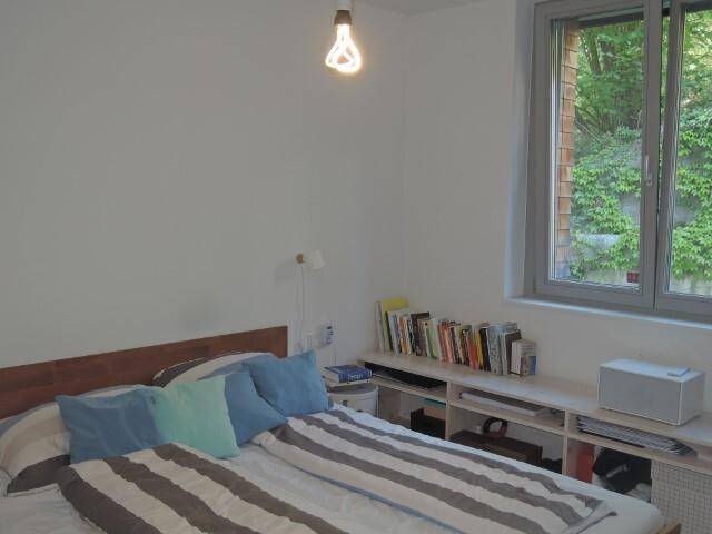 Gemütliches Schlafzimmer mit Holzbett, Bücherregal und einem Fenster mit Blick ins Grüne.