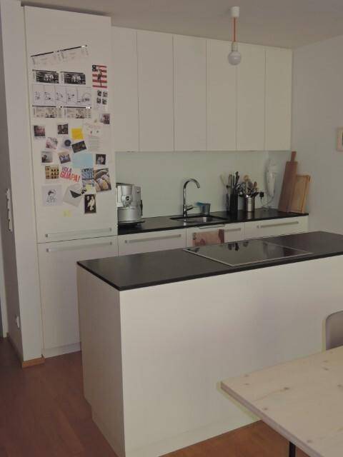 Moderne Einbauküche mit weißen Schränken, dunklen Arbeitsplatten und einer Kochinsel.