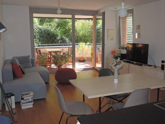 Geräumiger Wohnbereich mit bequemer Couch, Esstisch und großen Fenstern zum grünen Balkon.
