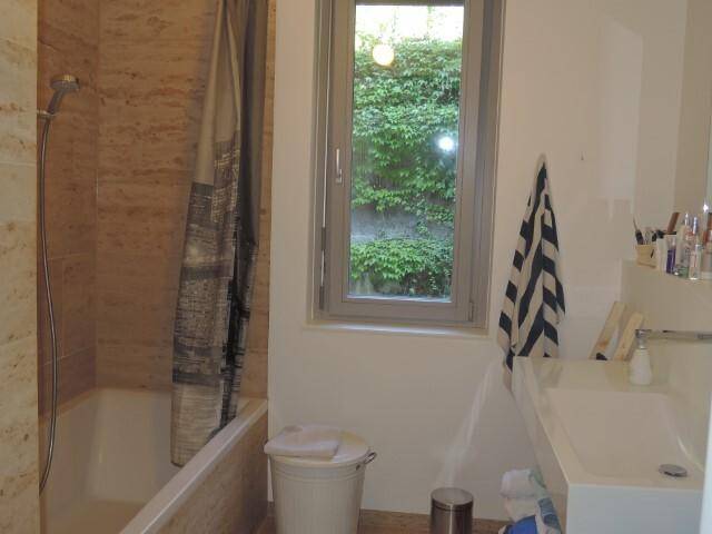Badezimmer mit Badewanne, Duschvorhang, Waschbecken und einem Fenster mit Blick auf Pflanzen.