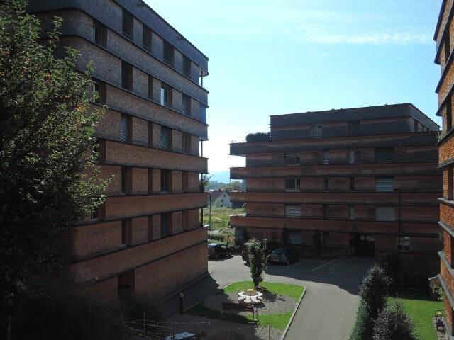 Ansicht eines modernen Wohnkomplexes mit mehreren Gebäuden, Parkplätzen und Grünflächen.
