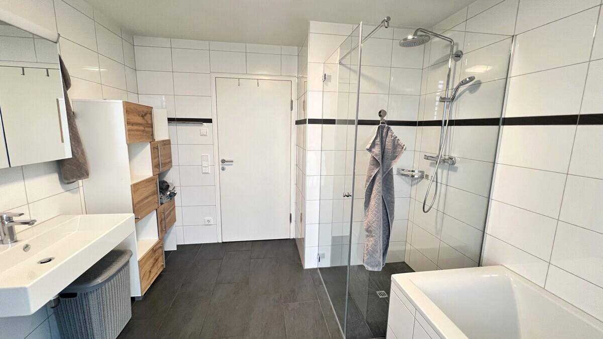 Geräumiges Badezimmer mit moderner begehbarer Dusche, Badewanne und Waschtisch, hell gefliest.