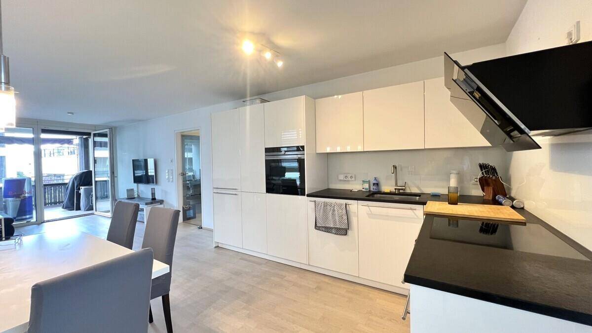 Moderne Einbauküche mit weißen Hochglanzfronten, dunkler Arbeitsplatte und integrierten Geräten in offenem Wohnbereich.