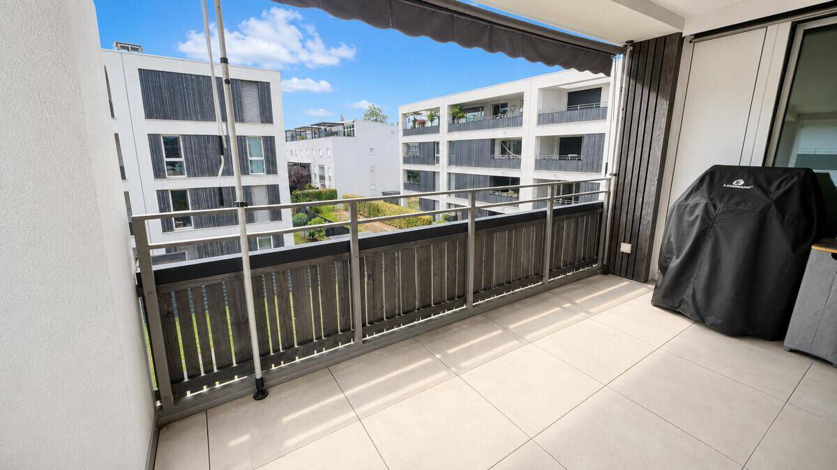 Geräumiger Balkon mit Fliesenboden und Blick auf die moderne Wohnanlage und Grünflächen.