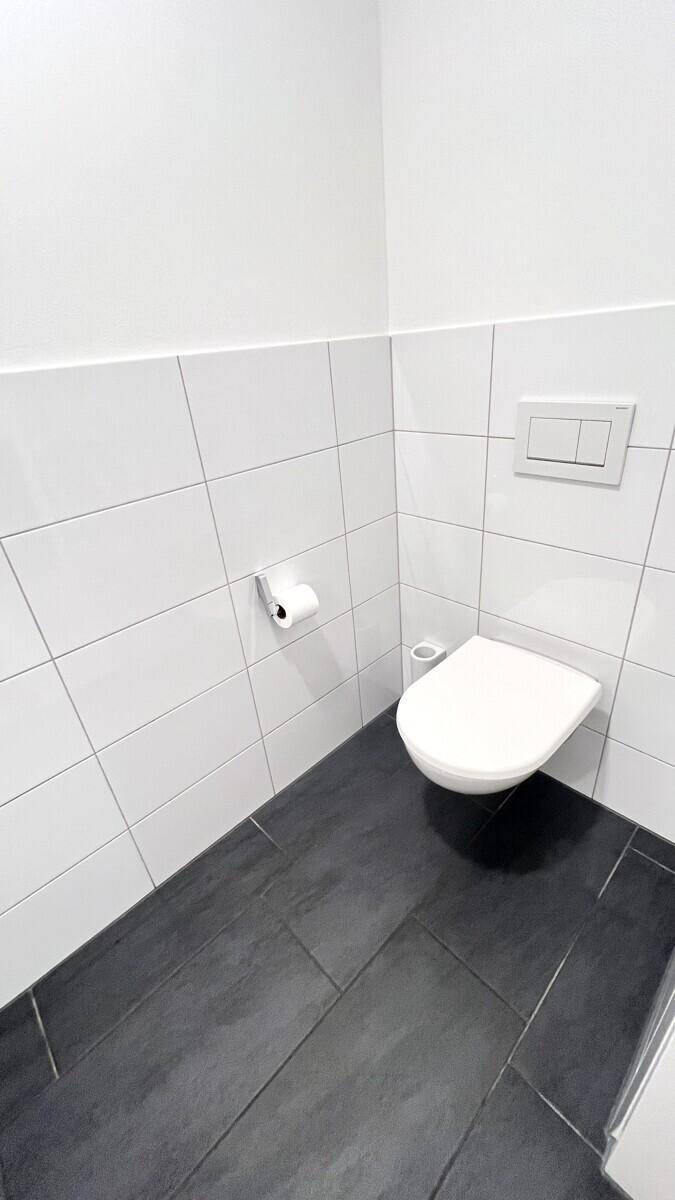 Separates Gäste-WC mit wandhängendem WC und modernen Fliesen in Weiß und Dunkelgrau.