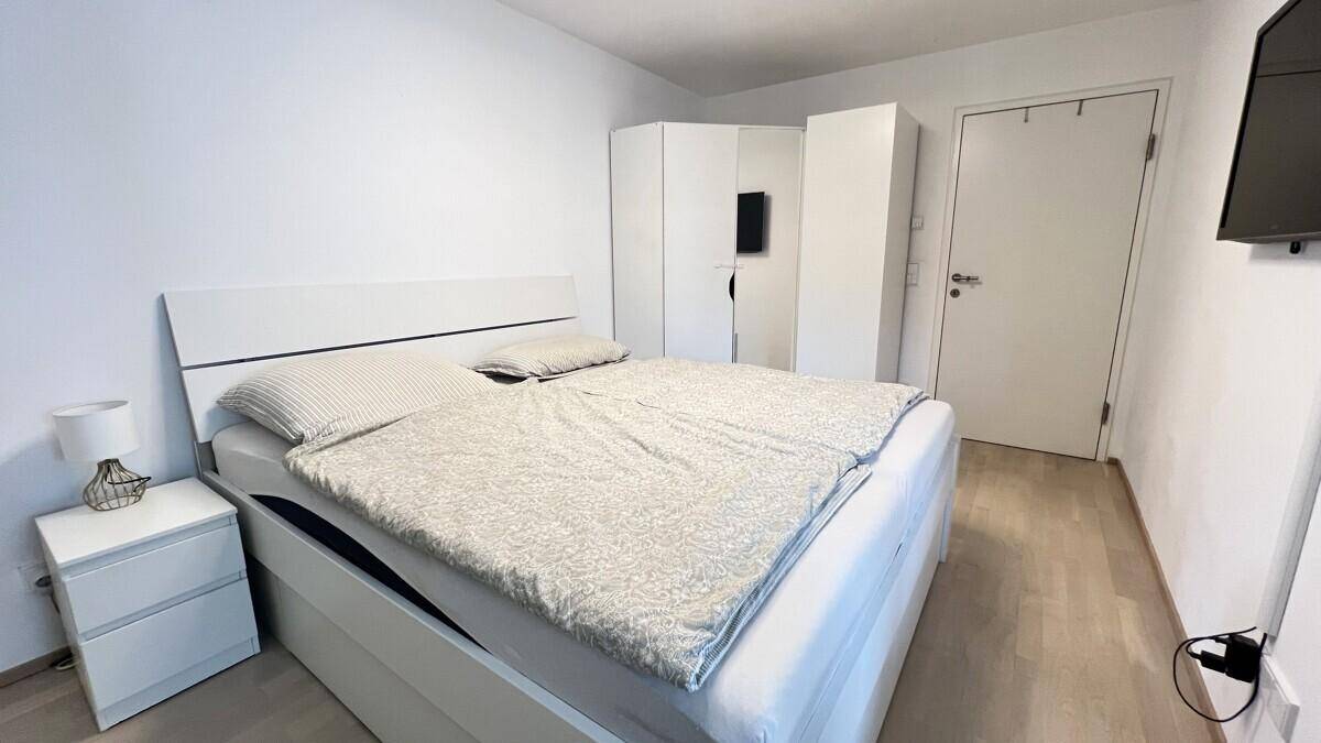 Helles Schlafzimmer mit modernem weißen Bett, Nachttisch und geräumigen Kleiderschränken.