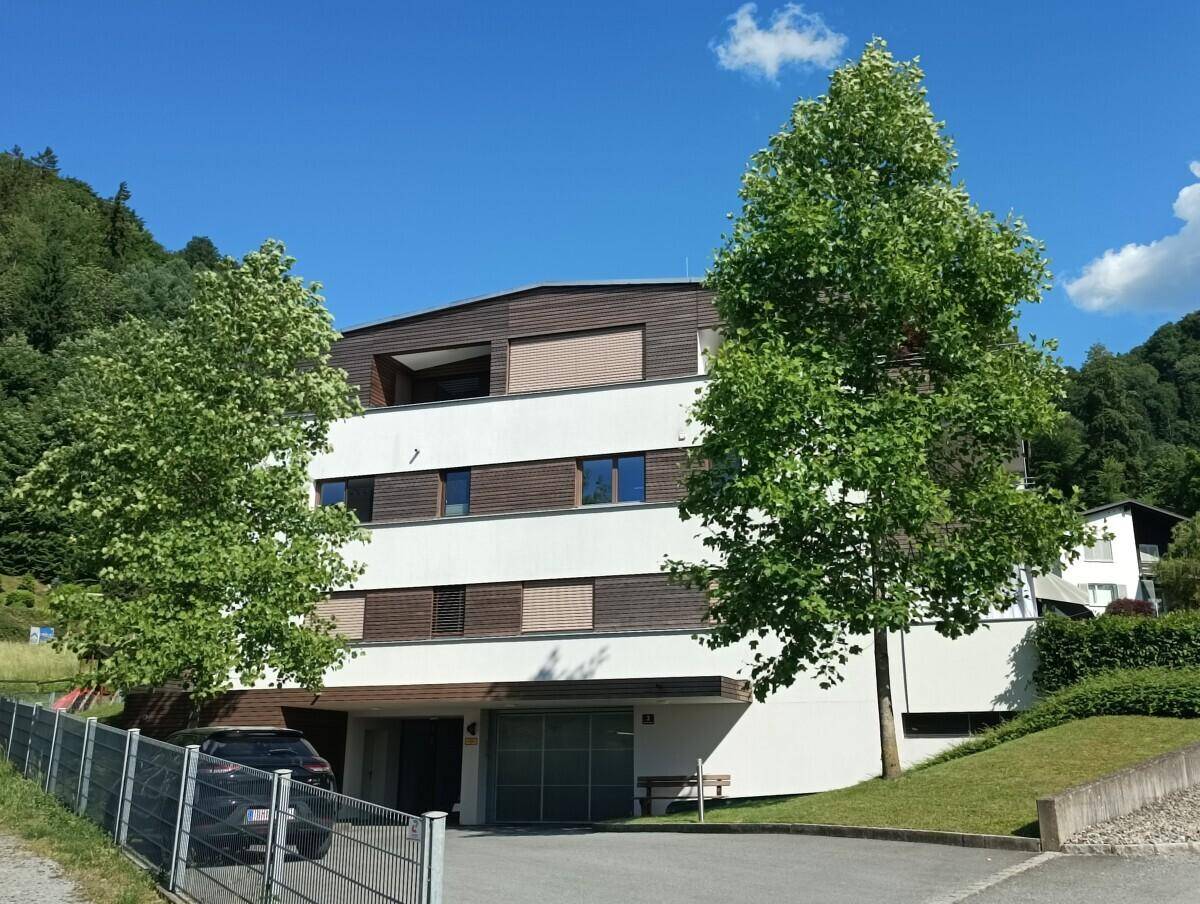 Modernes Mehrfamilienhaus mit weißer Fassade und Holzelementen, umgeben von viel Grün.