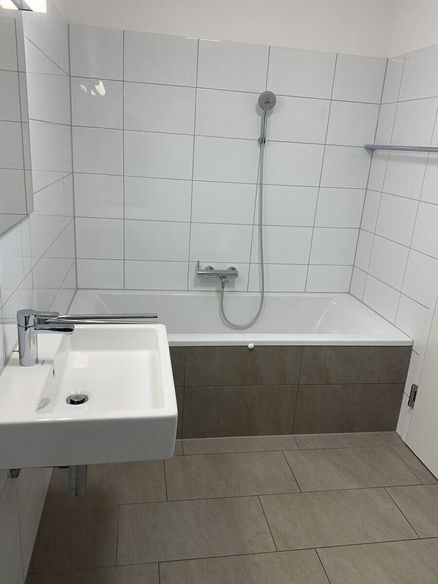 Helles Badezimmer mit Badewanne, modernem Waschbecken und großen Wandfliesen.