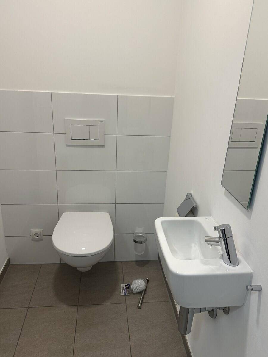 Separates Gäste-WC mit Wand-WC, kleinem Waschbecken und hellen Fliesen.