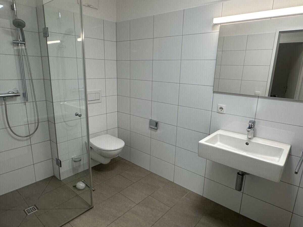 Modernes Badezimmer mit ebenerdiger Dusche, Wand-WC und weißen Fliesen.
