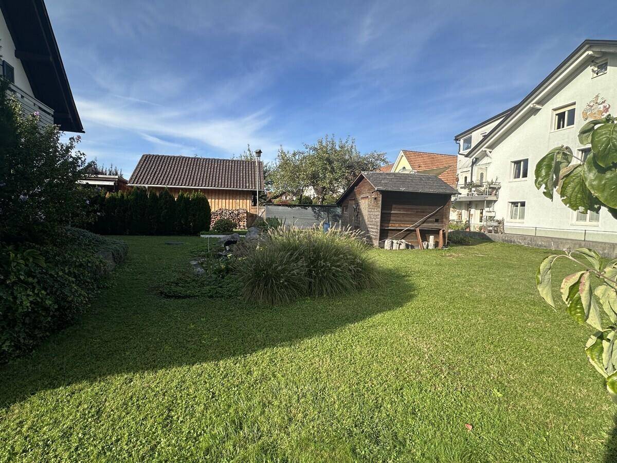 Großer, sonniger Garten mit Rasenfläche, Gartenhaus und hohen Hecken im Hintergrund.