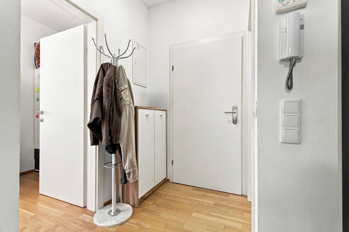 Heller Flur mit Holzparkettboden, Garderobe und weiß gestrichenen Wänden.