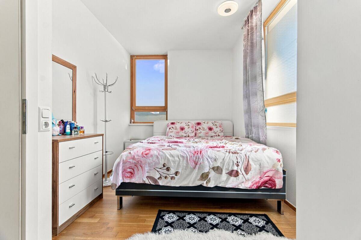 Helles Schlafzimmer mit floraler Bettwäsche, Holzkommode und Holzboden.