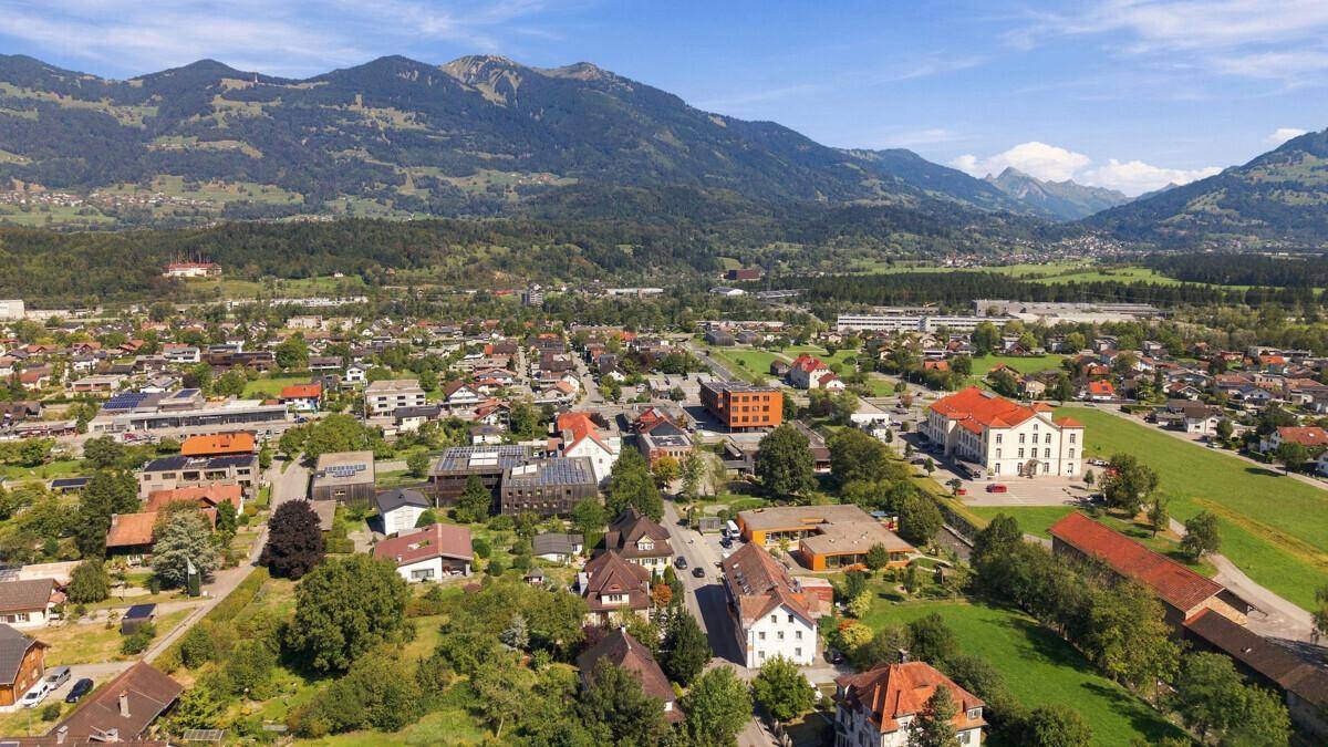 Panoramablick aus der Vogelperspektive auf eine Siedlung umgeben von grünen Bergen.
