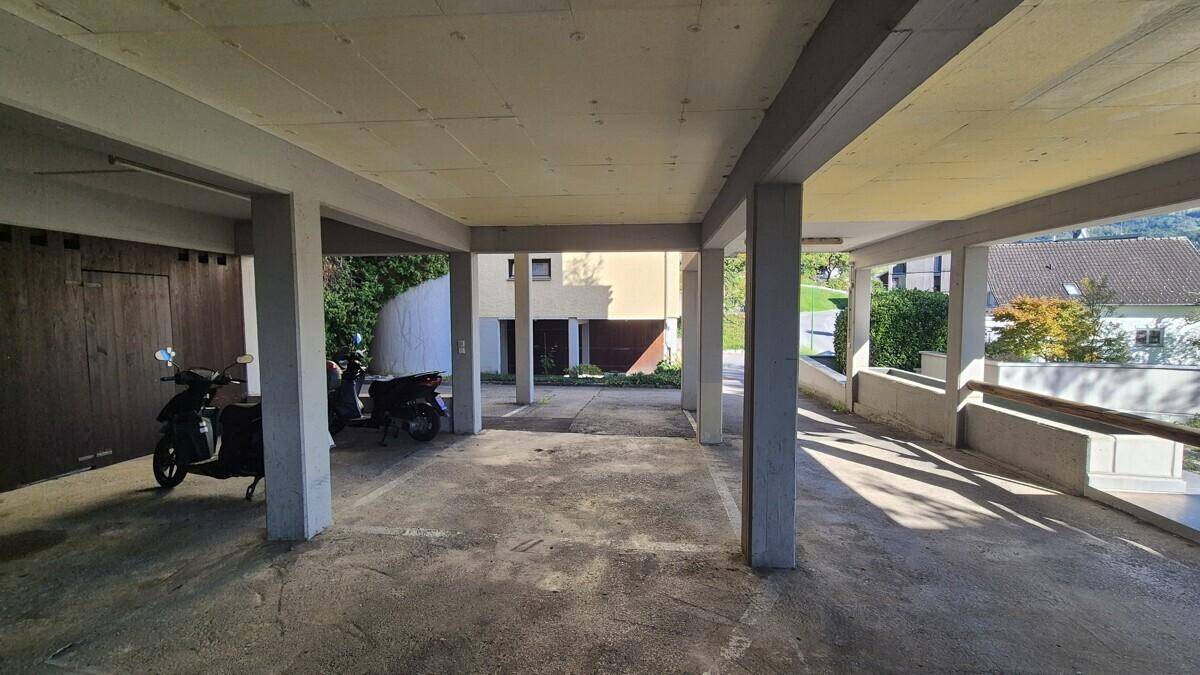 Offener Parkbereich mit Betonstützen, angrenzenden Garagen und Blick ins Grüne.