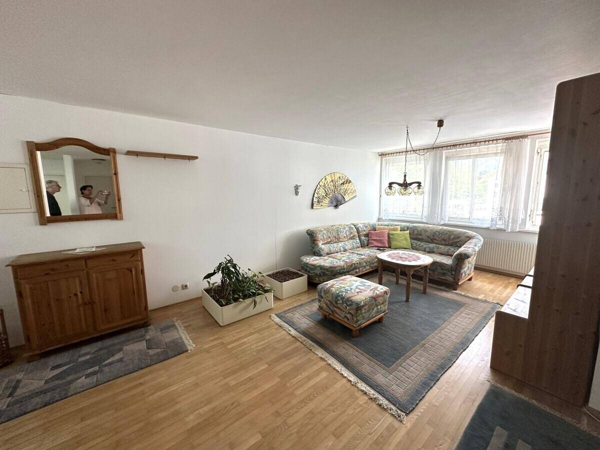 Gemütliches Wohnzimmer mit Holzfußboden, bequemer Couch und Fenster mit Vorhängen.