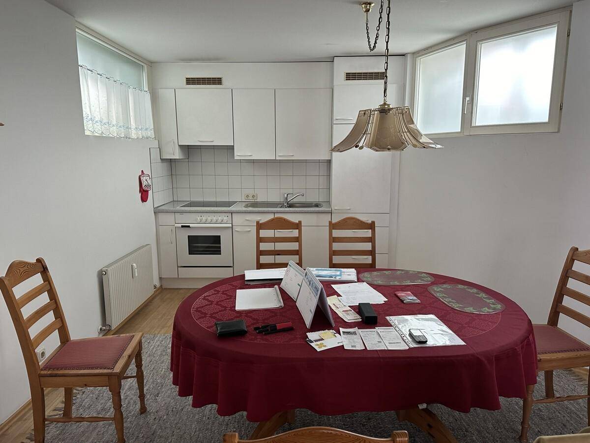 Kleine Küche mit weißer Einbauküche, Esstisch und Stühlen, ideal für Mahlzeiten.