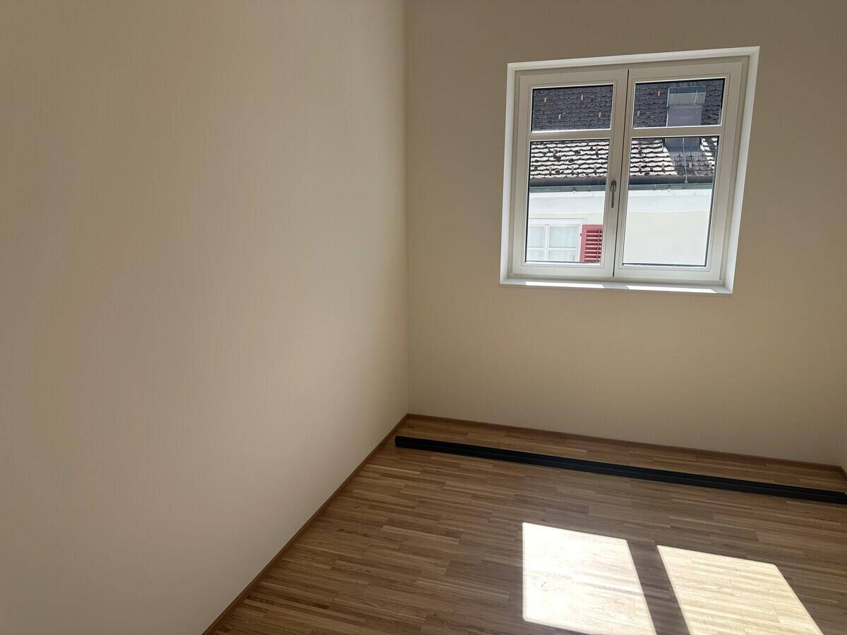 Heller Raum mit Holzfußboden und einem Fenster, das viel Tageslicht hereinlässt.