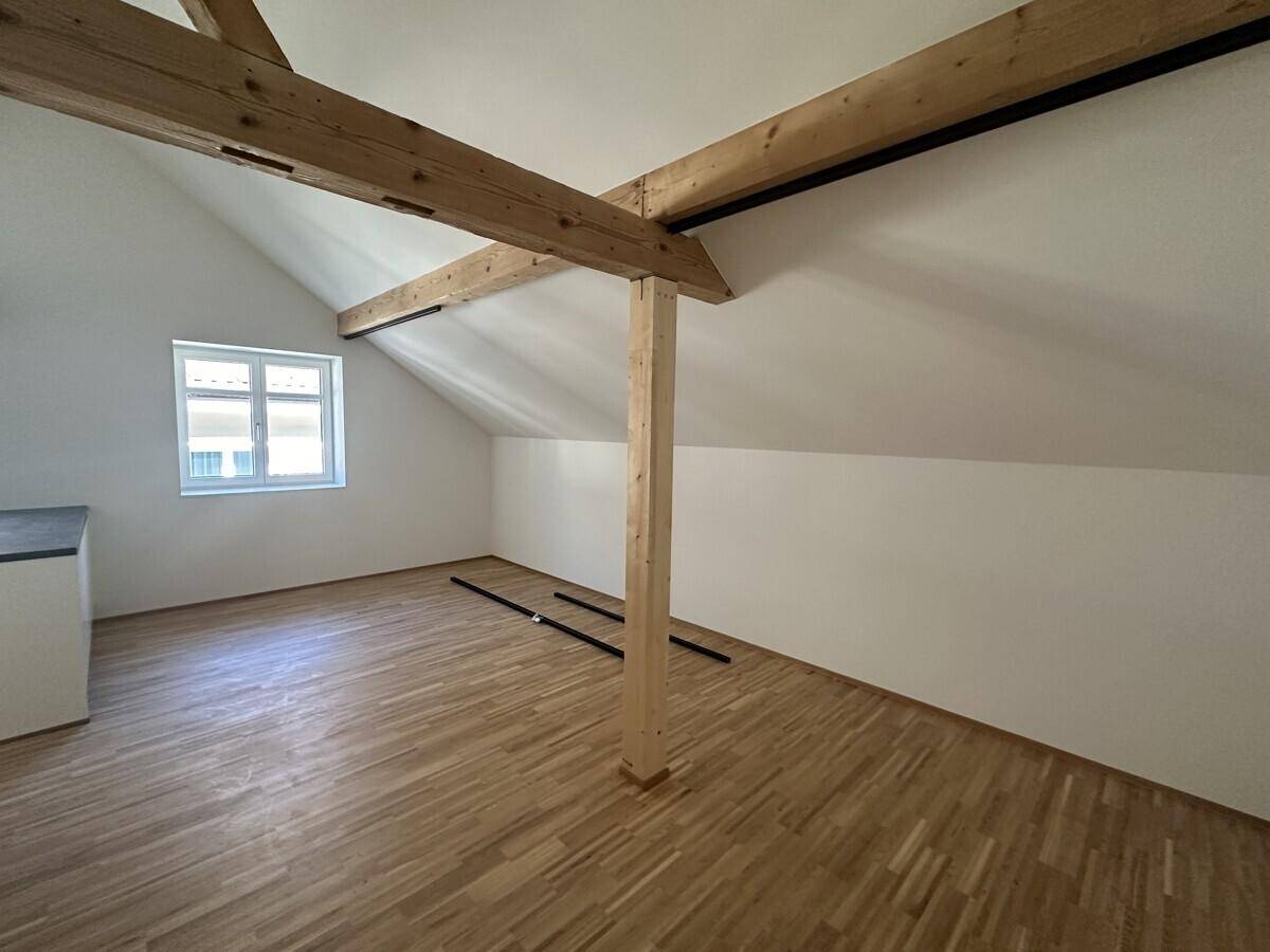Heller Dachbodenraum mit sichtbaren Holzbalken, Schrägdach und neuem Holzfußboden.