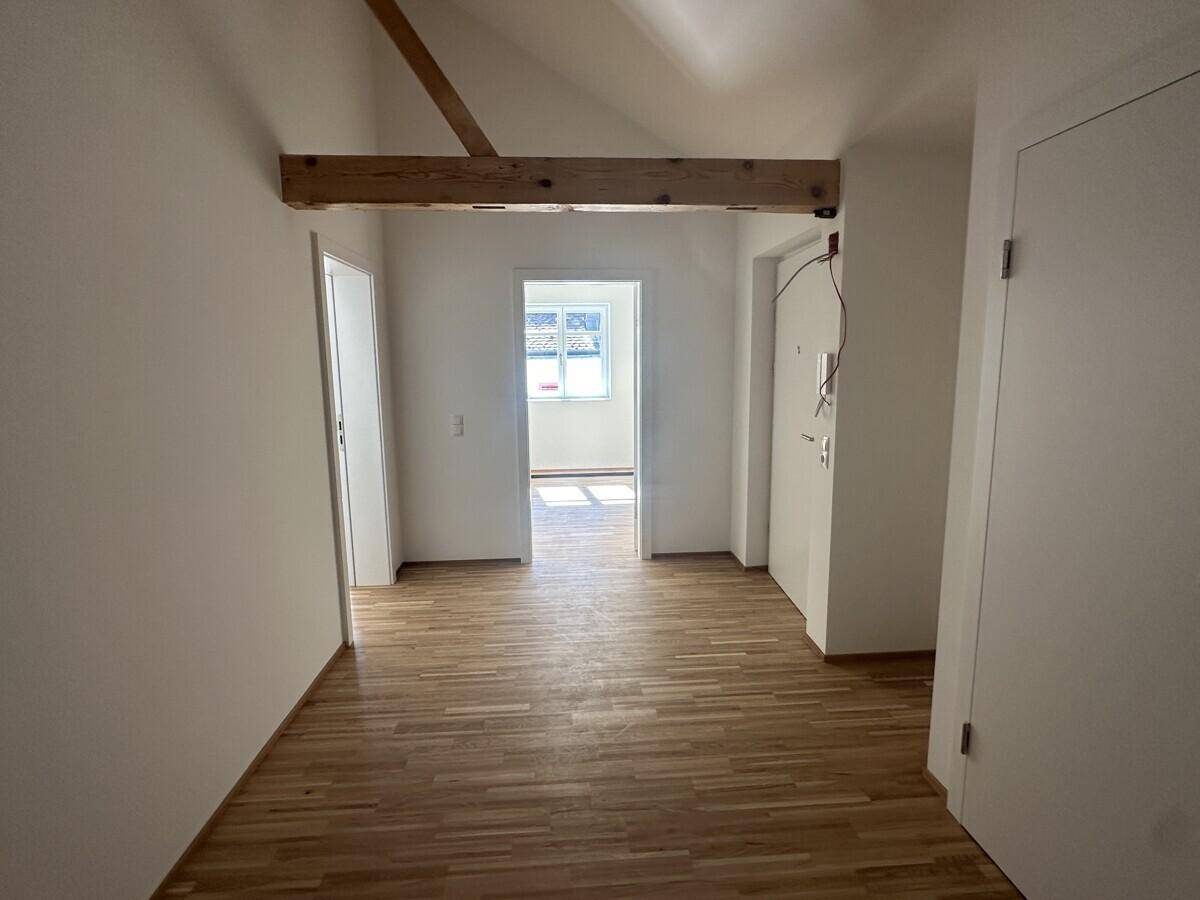 Heller Flur mit Holzfußboden und sichtbarem Holzbalken, der zu weiteren Räumen führt.