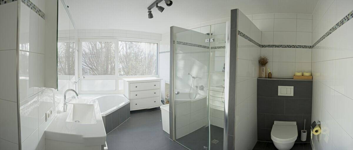 Modernes Badezimmer mit Badewanne, begehbarer Dusche, WC und großem Fenster.