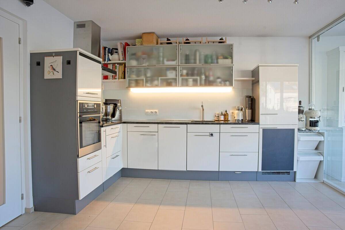 Moderne Küche mit weißen und grauen Schränken, integrierten Geräten und Fliesenboden.