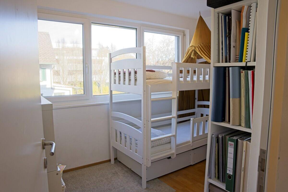 Kinderzimmer mit weißem Etagenbett, Bücherregal und großem Fenster für viel Tageslicht.