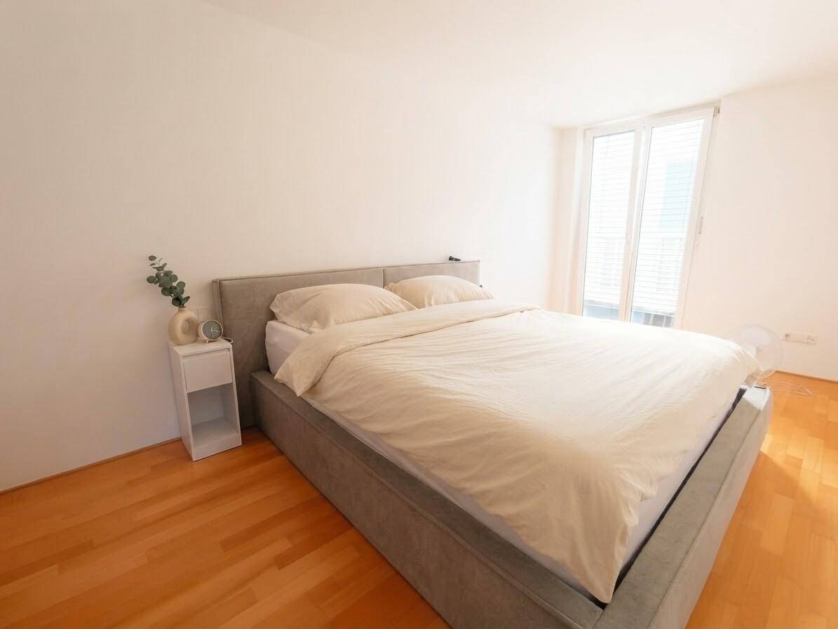 Helles Schlafzimmer mit Doppelbett, Holzboden und Fenster mit Rollläden für angenehme Ruhe.
