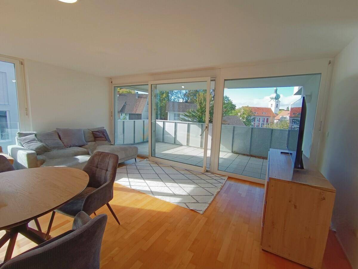 Heller Wohn-Essbereich mit Holzboden, gemütlichem Sofa und Zugang zu einem großen Balkon mit Stadtblick.