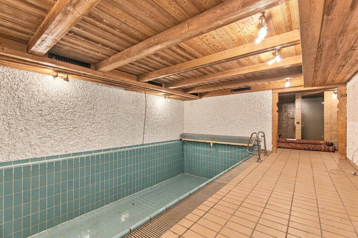 Exklusiver Innenpoolbereich mit gefliestem Becken und rustikaler Holzdeckenverkleidung für Entspannung.
