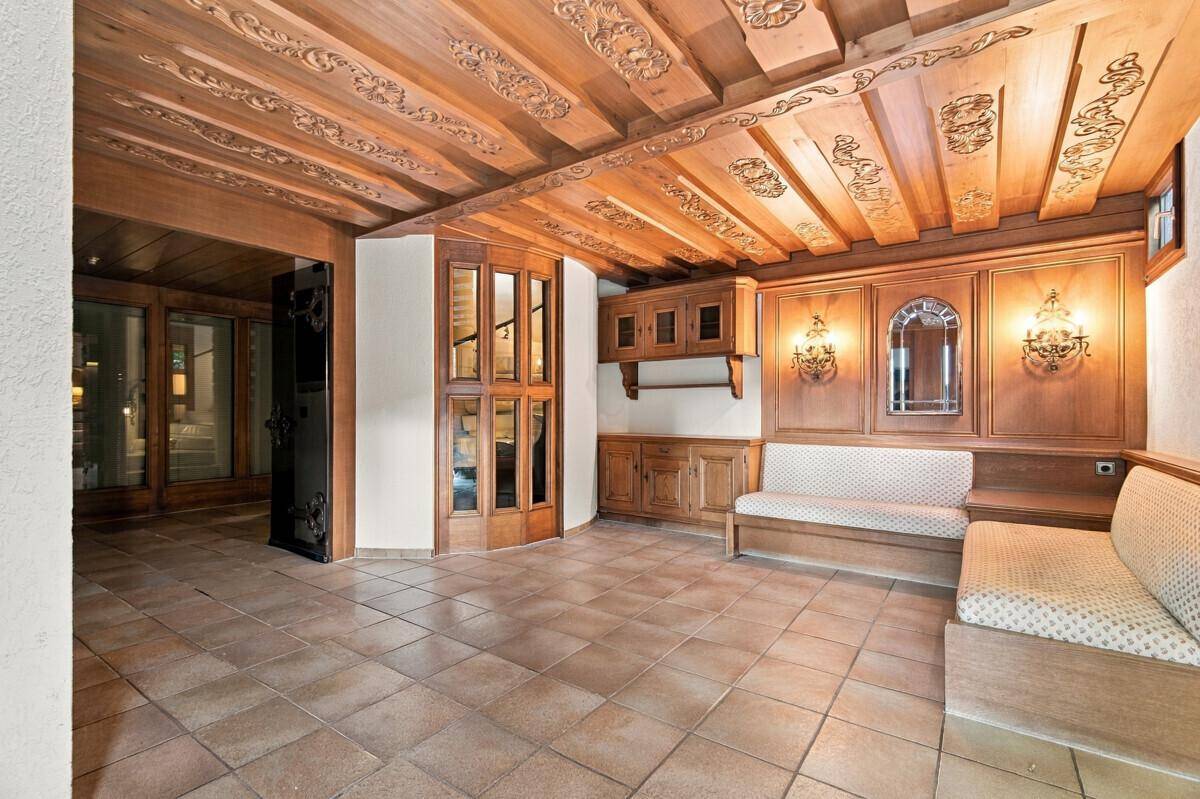 Traditioneller Eingangsbereich mit aufwendig geschnitzter Holzdecke, gefliestem Boden und Sitzgelegenheiten.