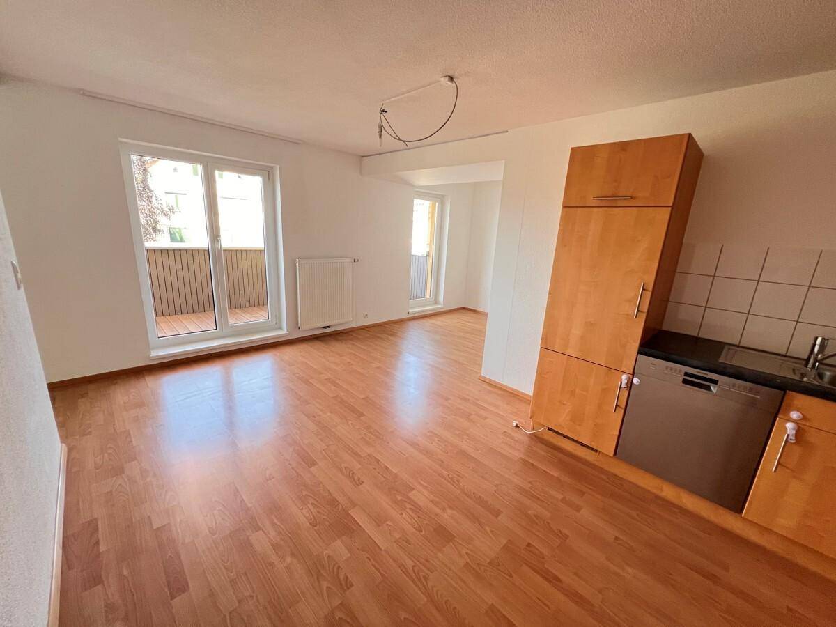Heller Wohnbereich mit Holzboden, Zugang zum Balkon und integrierter Küchenzeile.