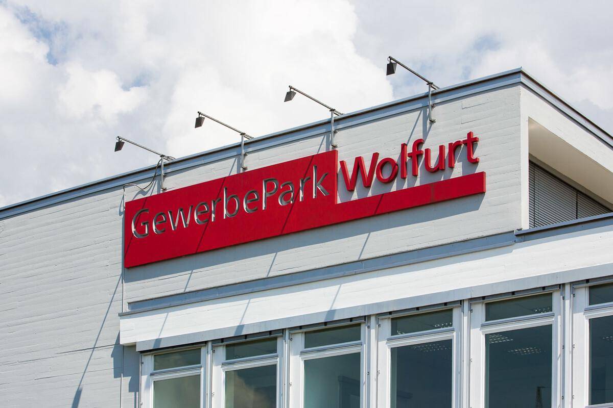 Nahaufnahme der Gebäudefassade mit einem großen roten Schild "GewerbePark Wolfurt" und weißen Fenstern.