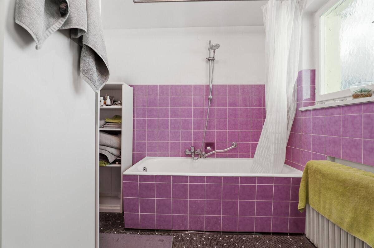 Badezimmer mit lila Fliesen, Badewanne und Fenster, das für Belüftung sorgt.