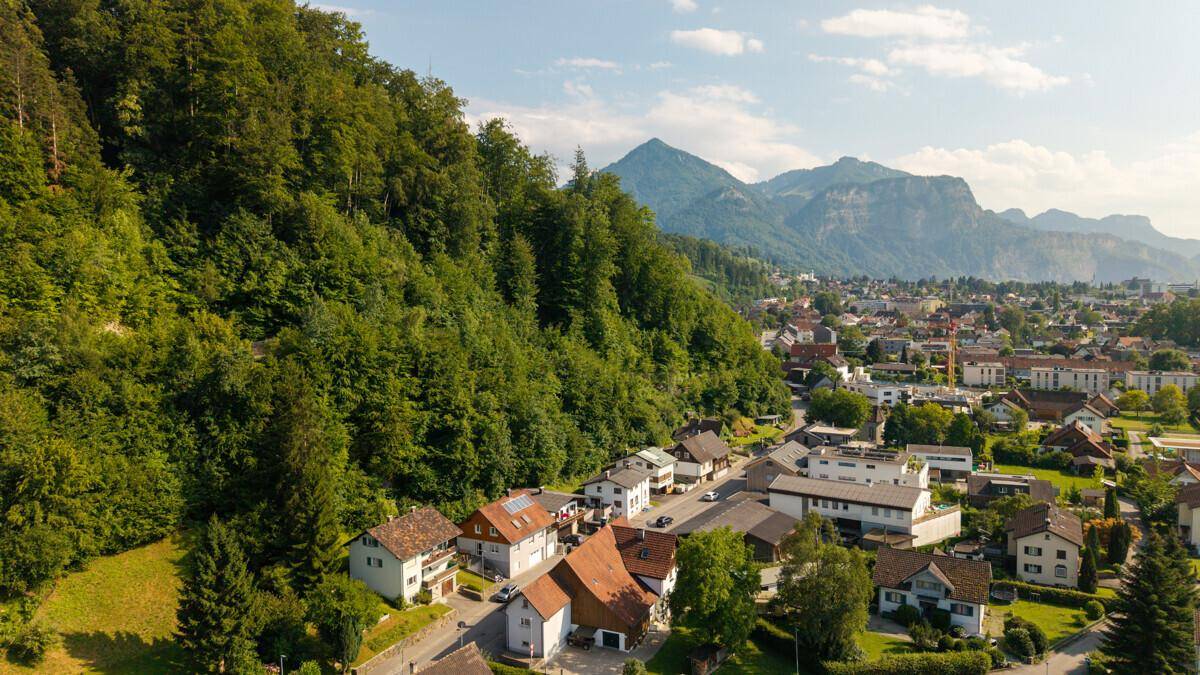 Panoramablick auf die Stadt, eingebettet in eine grüne Hügellandschaft mit majestätischen Bergen im Hintergrund.