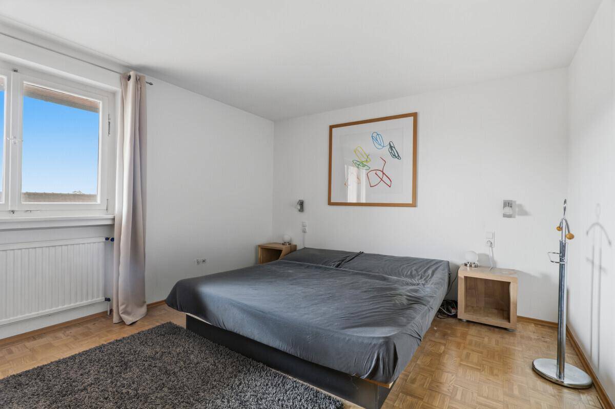 Schlafzimmer mit Doppelbett, Parkettboden und großem Fenster für viel Tageslicht.