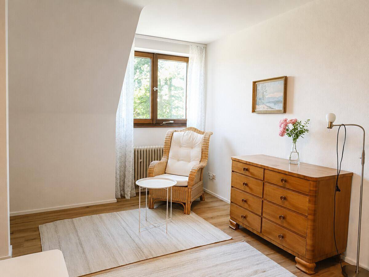 Gemütliches Zimmer mit Dachschräge, Korbsessel und Holzkommode, hell und freundlich gestaltet.