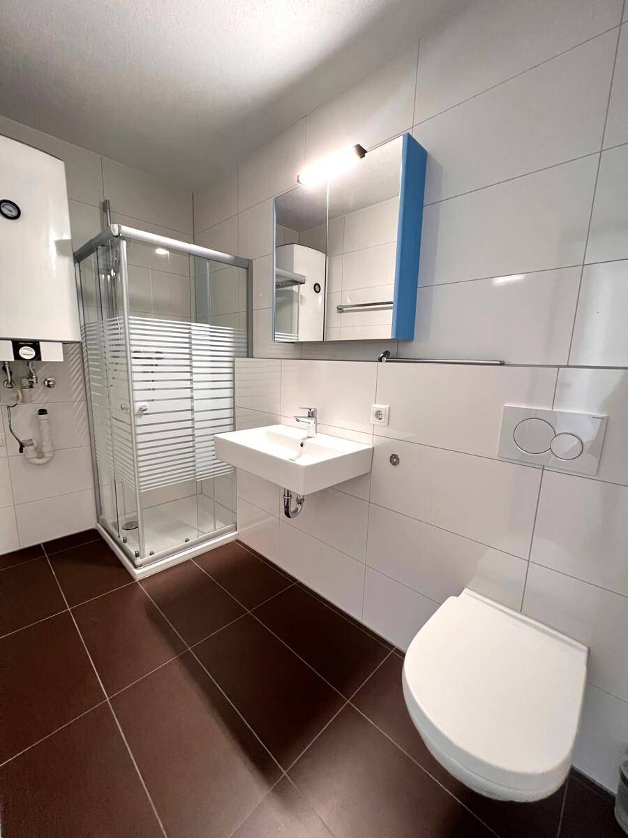 Modernes Badezimmer mit Duschkabine, Waschbecken, WC und braunen Bodenfliesen.