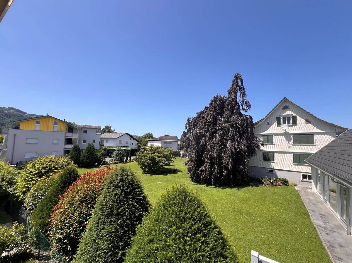 Gepflegter Gemeinschaftsgarten mit Rasenflächen, Bäumen und Blick auf umliegende Häuser.