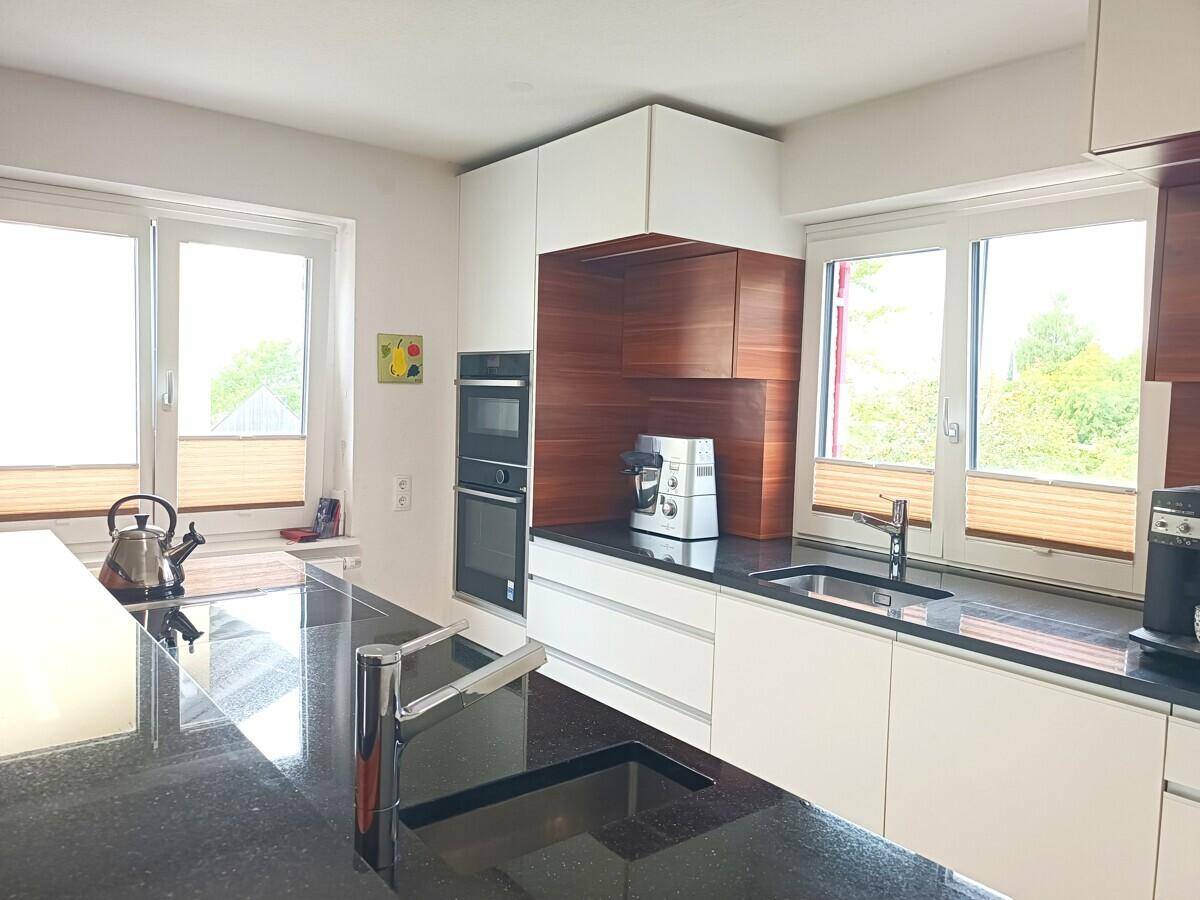 Helle Küche mit großen Fenstern, moderner Ausstattung und viel Arbeitsfläche auf der Kücheninsel.