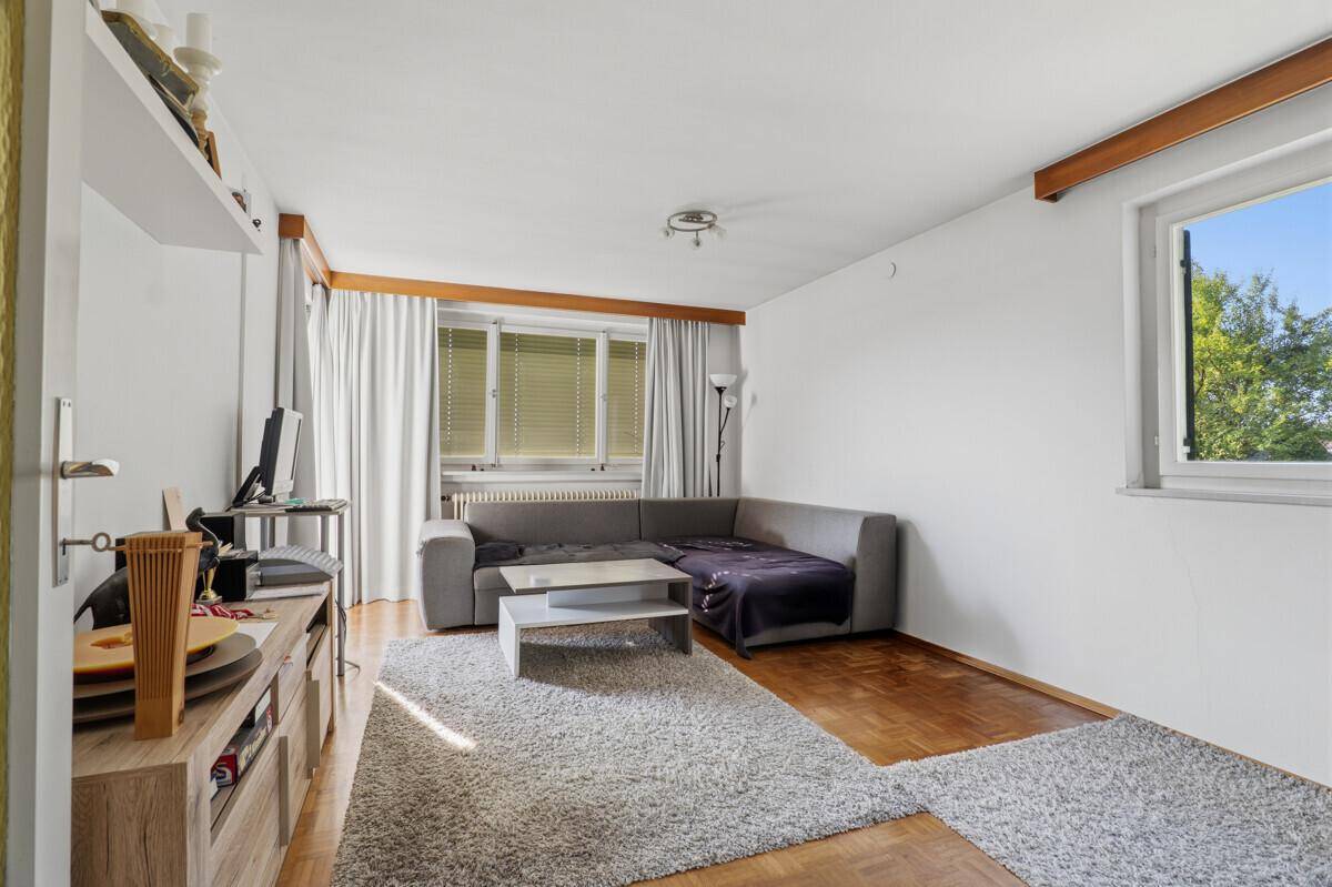 Gemütliches Wohnzimmer mit grauem Ecksofa, Teppich und Parkettboden, hell und einladend.