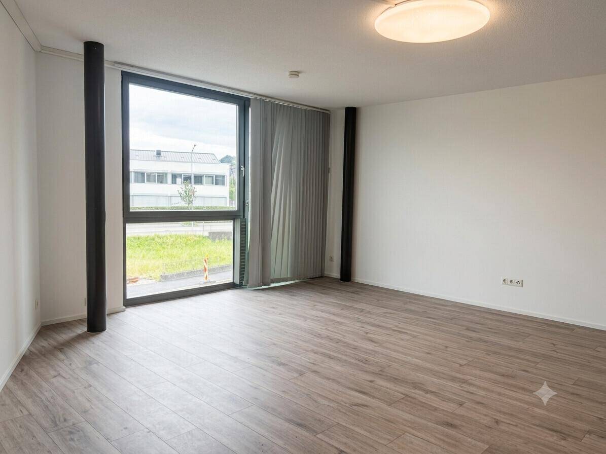 Heller, leerer Raum mit modernem Laminatboden und großen Fenstern mit Blick nach draußen.
