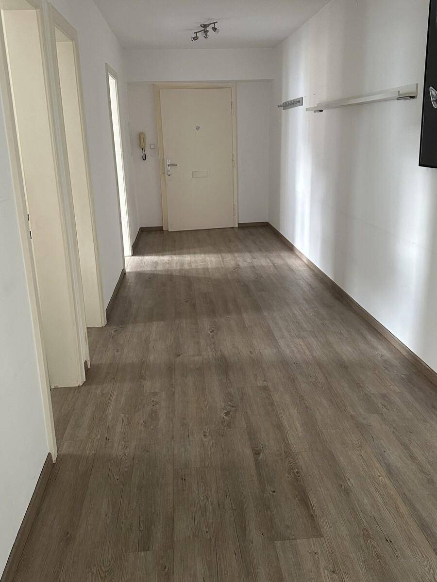 Heller Flur mit Laminatboden und weißer Eingangstür, der zu den Wohnräumen führt.