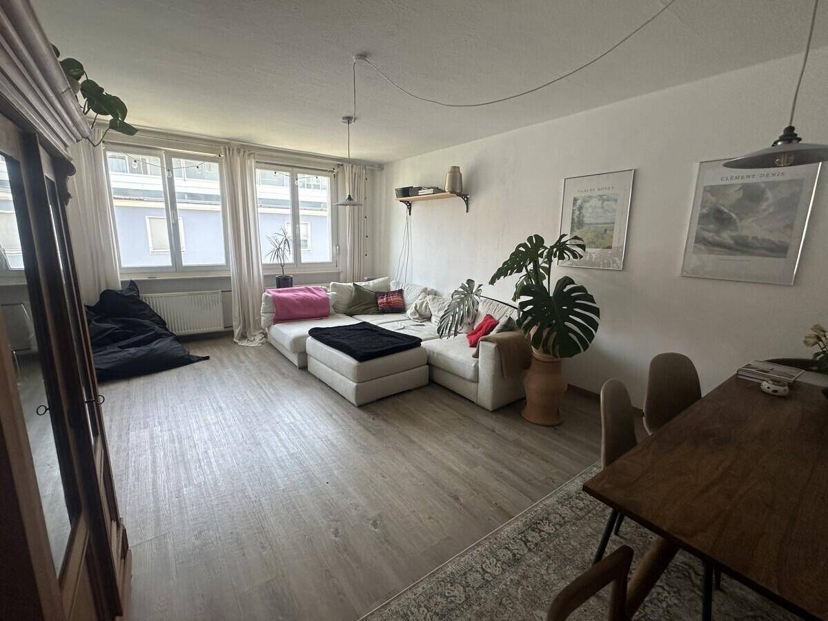 Helles Wohn-Esszimmer mit großem weißen Sofa, Holztisch und Laminatboden.
