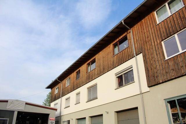 Seitenansicht des Gebäudes mit Holzverkleidung und Fenstern unter blauem Himmel.