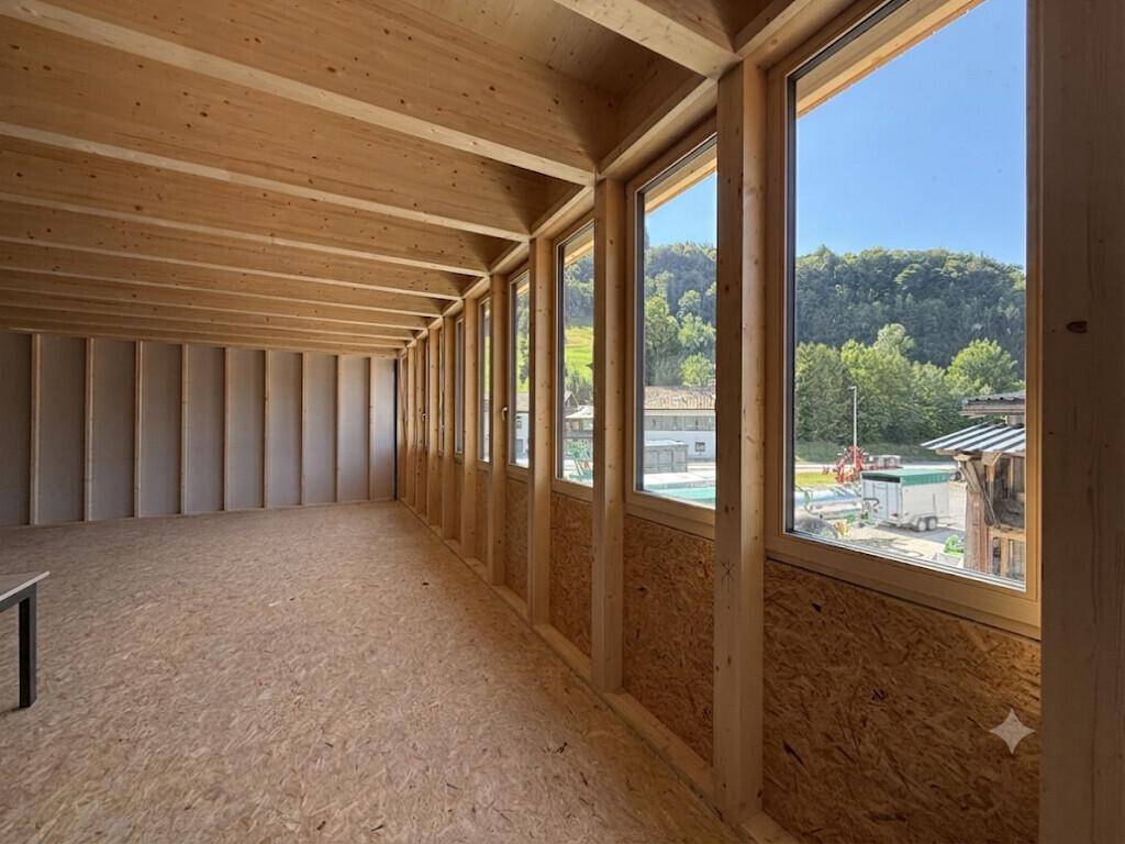 Unfertiger Innenraum mit Holzkonstruktion, OSB-Platten und großen Fenstern mit Blick ins Grüne.