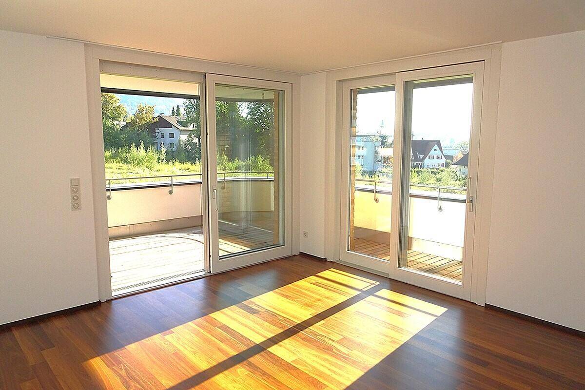 Lichtdurchfluteter Wohnbereich mit Holzboden und mehreren Schiebetüren, die zu einem Balkon führen.