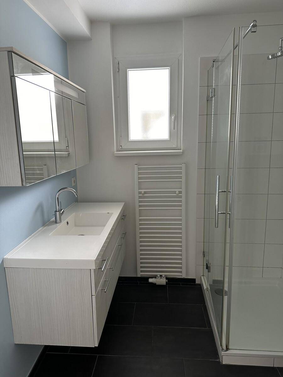 Modernes Badezimmer mit Dusche, Einzelwaschbecken, Spiegelschrank und beheiztem Handtuchhalter.