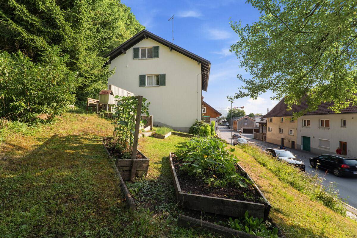 Terrassierter Garten mit Hochbeeten und Blick auf das Haus und die Straße.